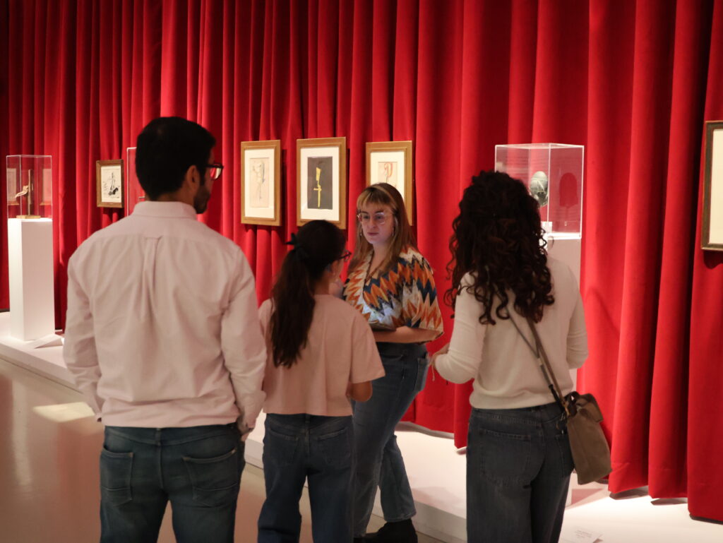 Grupo de jóvenes conversa en una sala de exposición con cortinas rojas