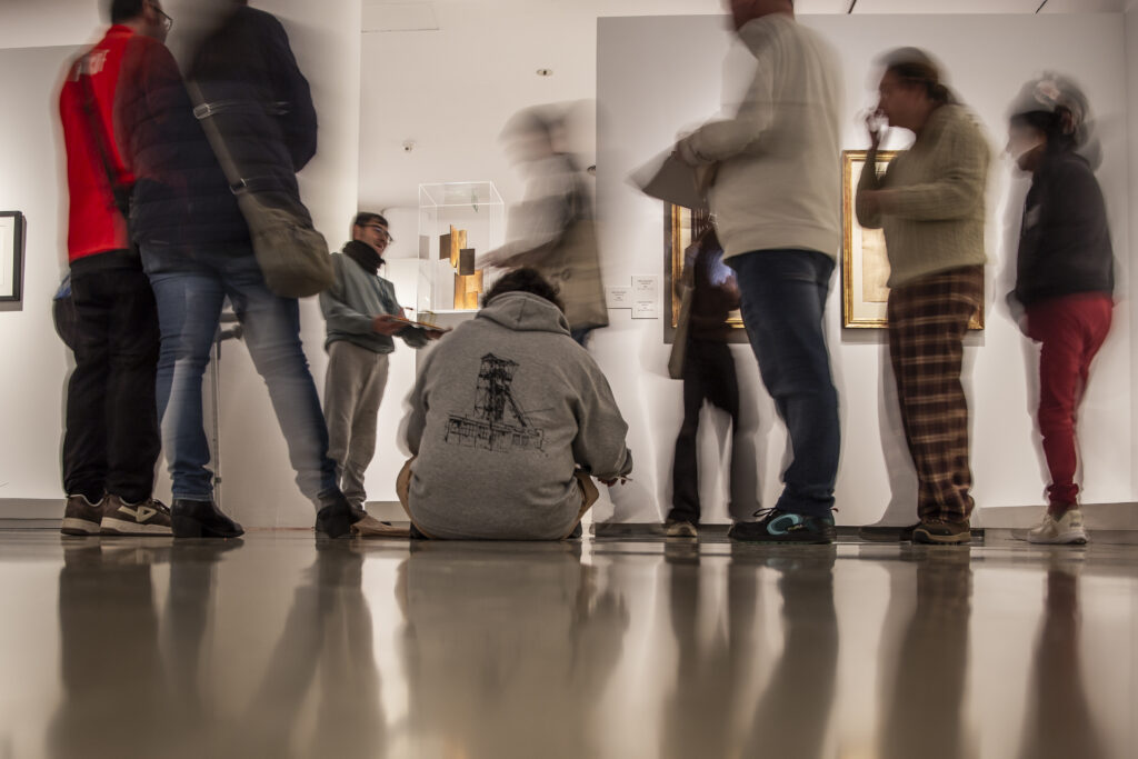 Visitantes recorren una sala de exposición y observan las obras de las paredes